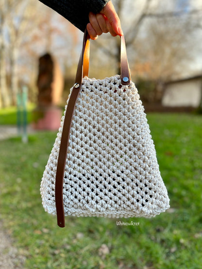 White woven macrame handbag with brown leather straps held by a person outdoors.