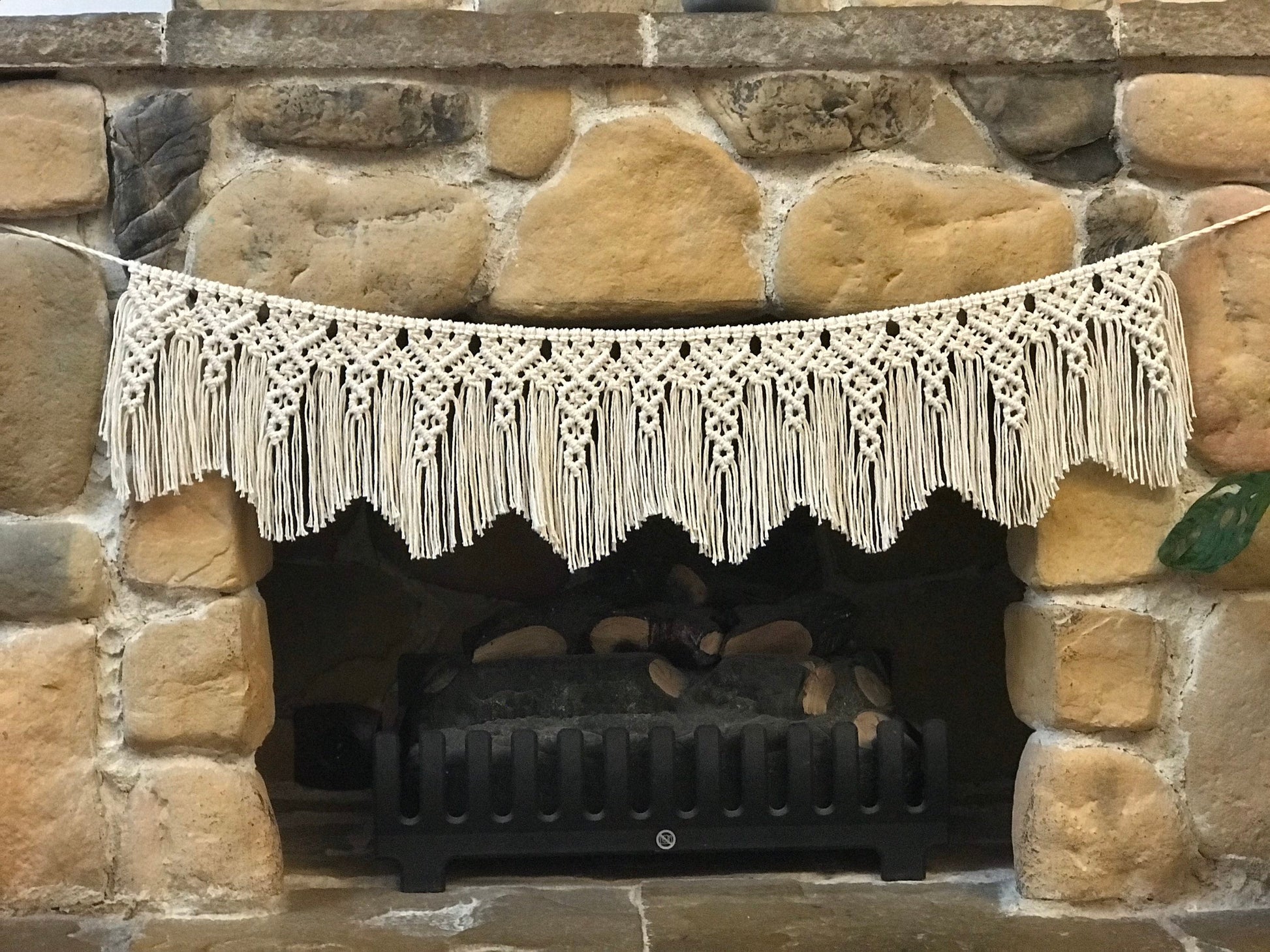 Macrame hanging above a stone fireplace with firewood inside