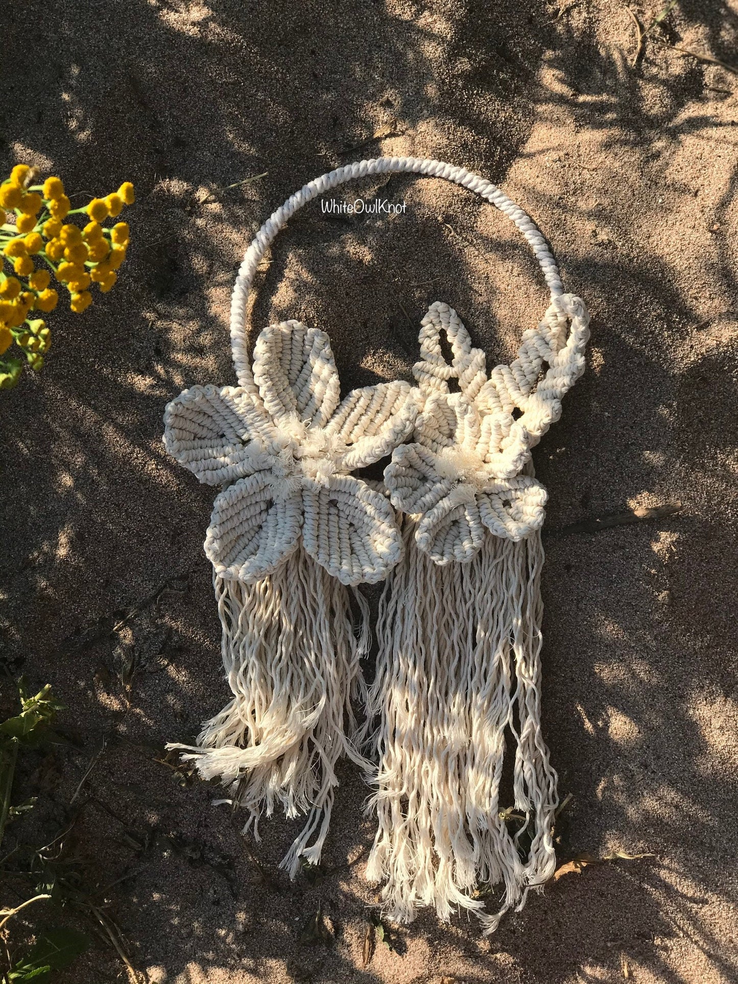 Macrame wall hanging with floral designs and tassels on a textured surface