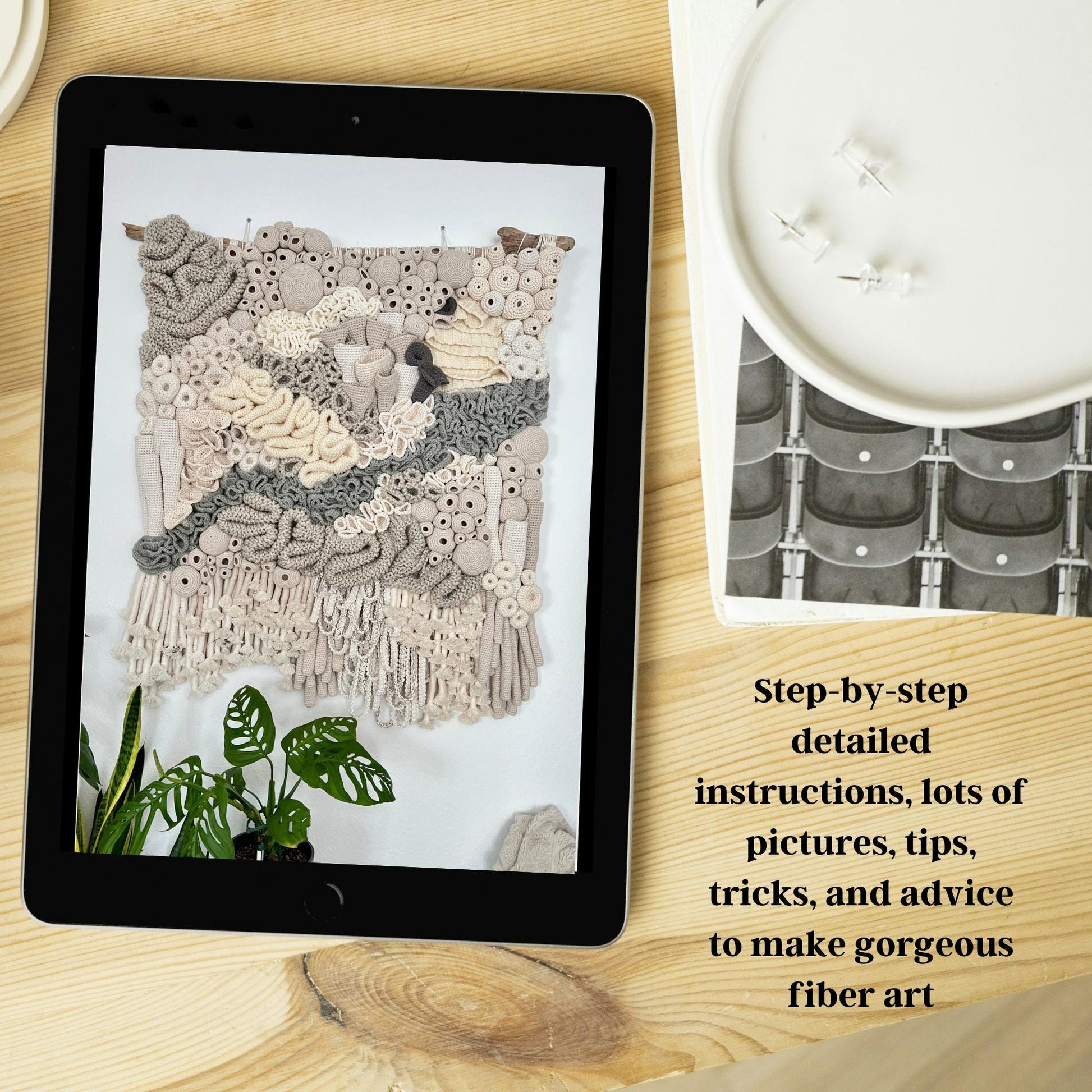 Tablet displaying fiber art on a wooden surface with text overlay