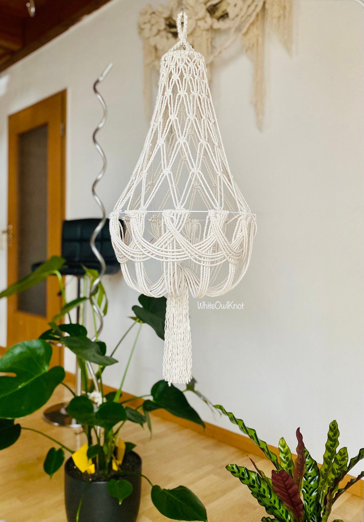 Macrame chandelier hanging in a room with plants and a door in the background.