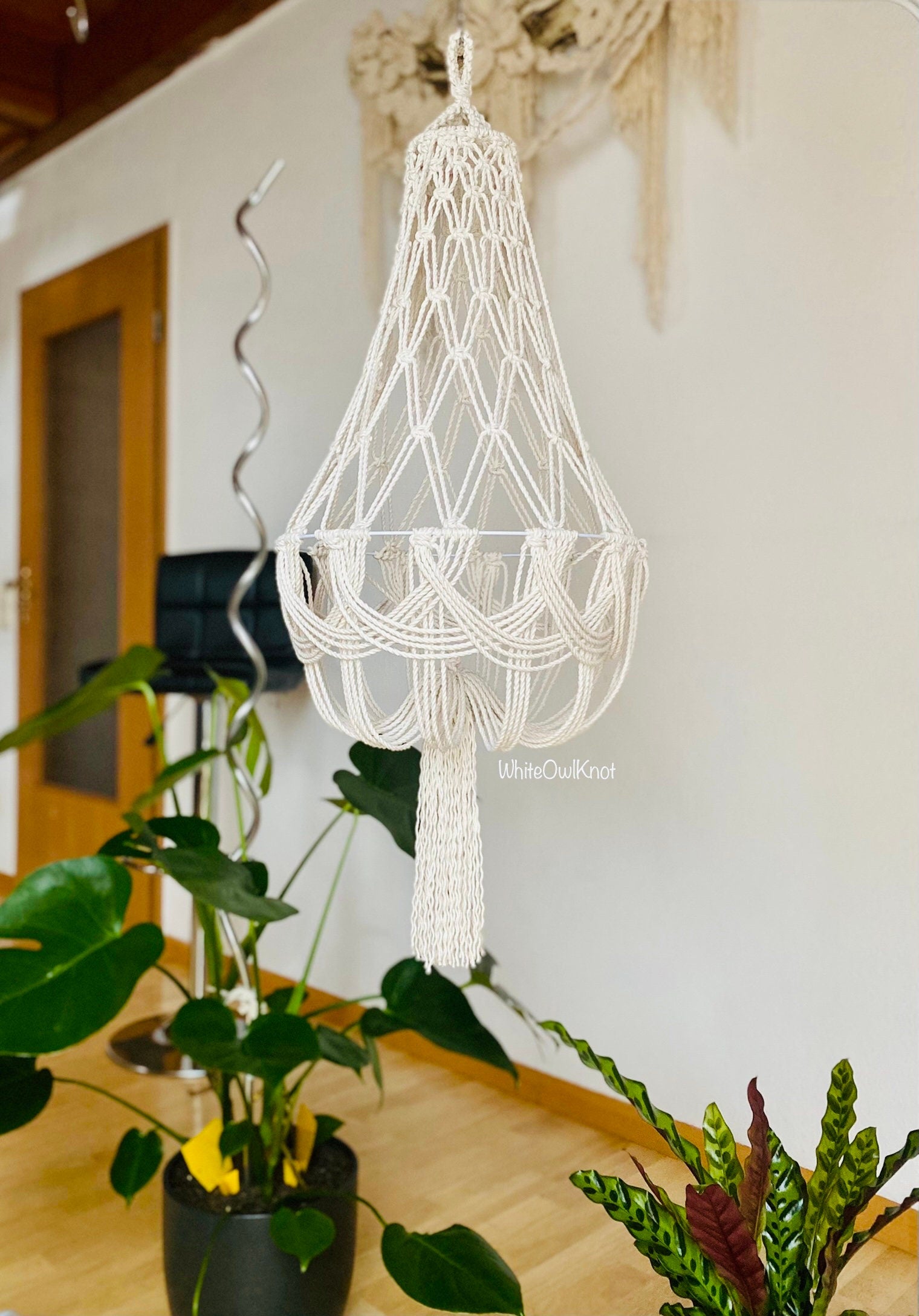 Macrame chandelier hanging in a room with plants and a door in the background.