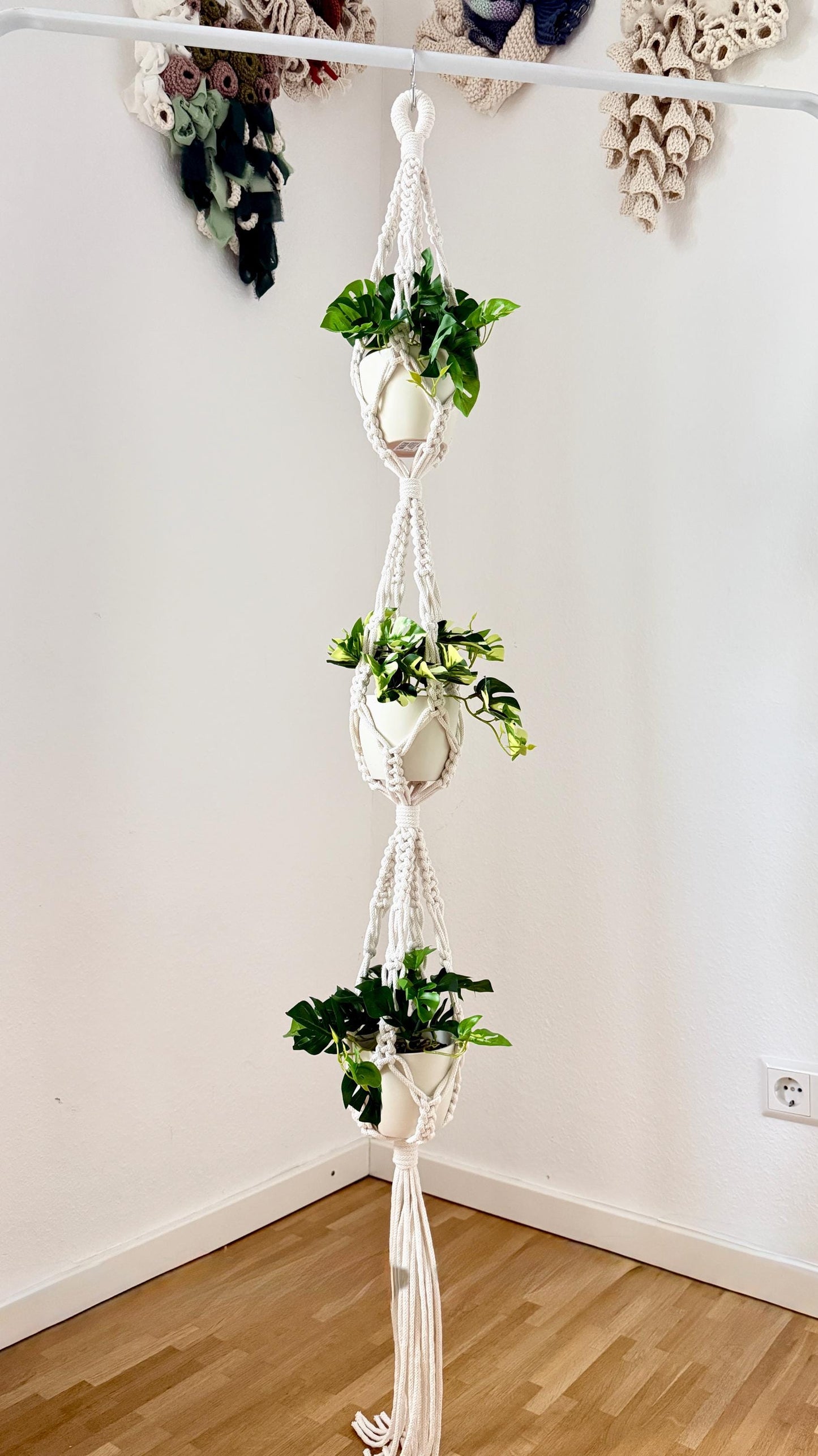 Macrame plant hanger with multiple plant pots against a white wall.