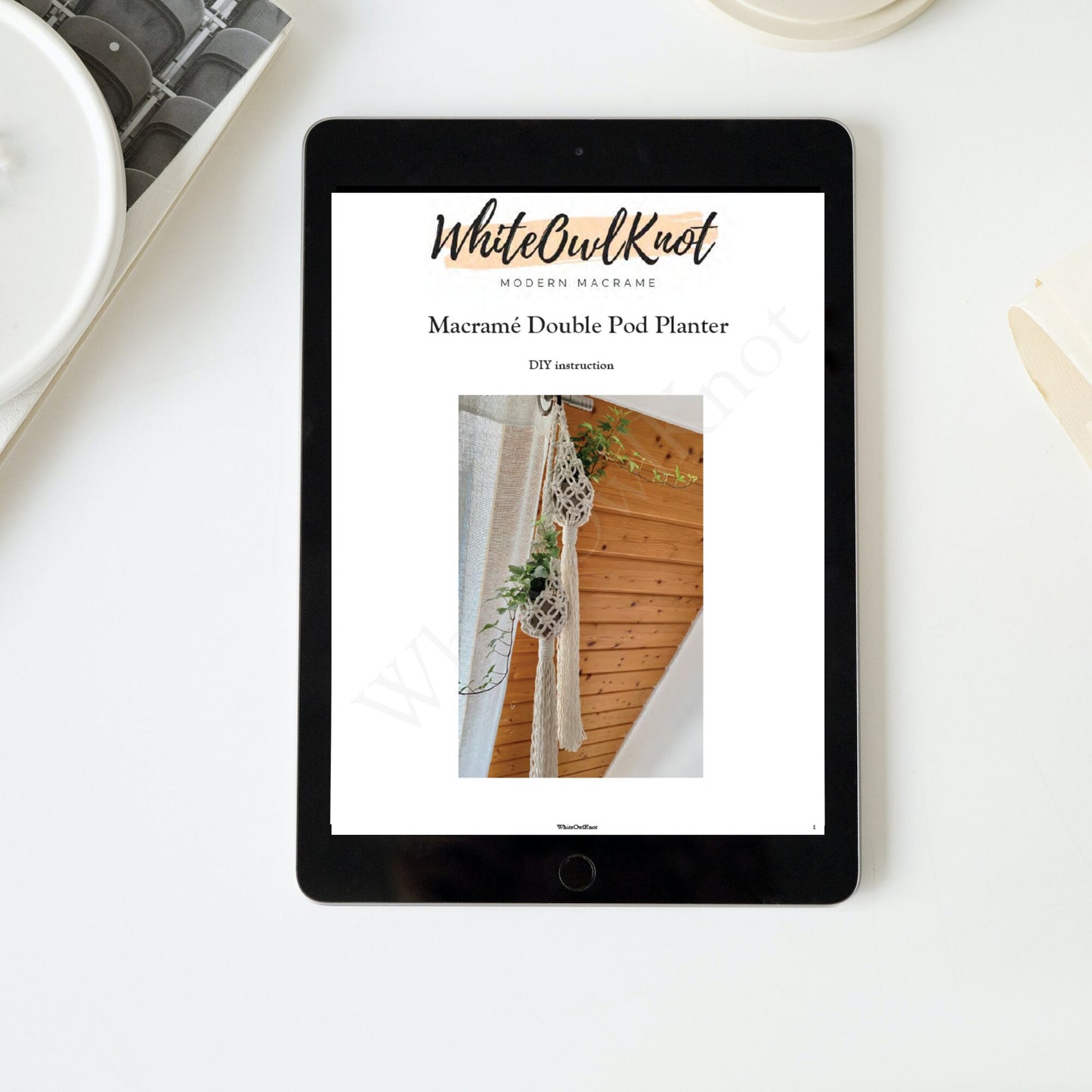 Tablet displaying a WhiteOwlKnot macrame double pod planter tutorial on a white surface.