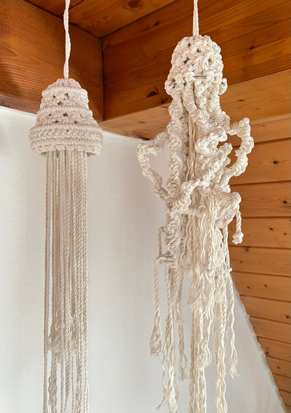 Two macrame jekkyfish hanging against a wooden ceiling.