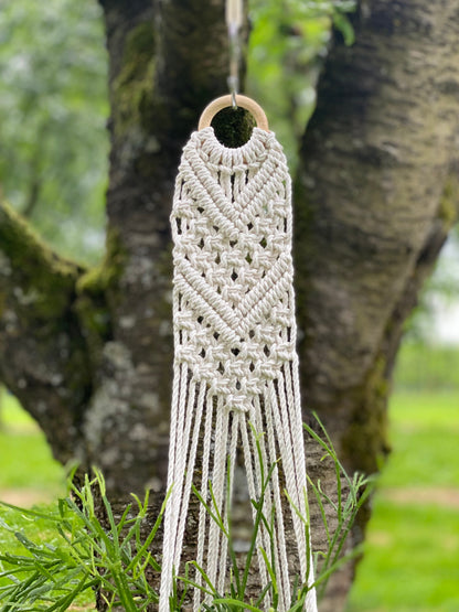 Macrame wall hanging hanging from a tree branch outdoors