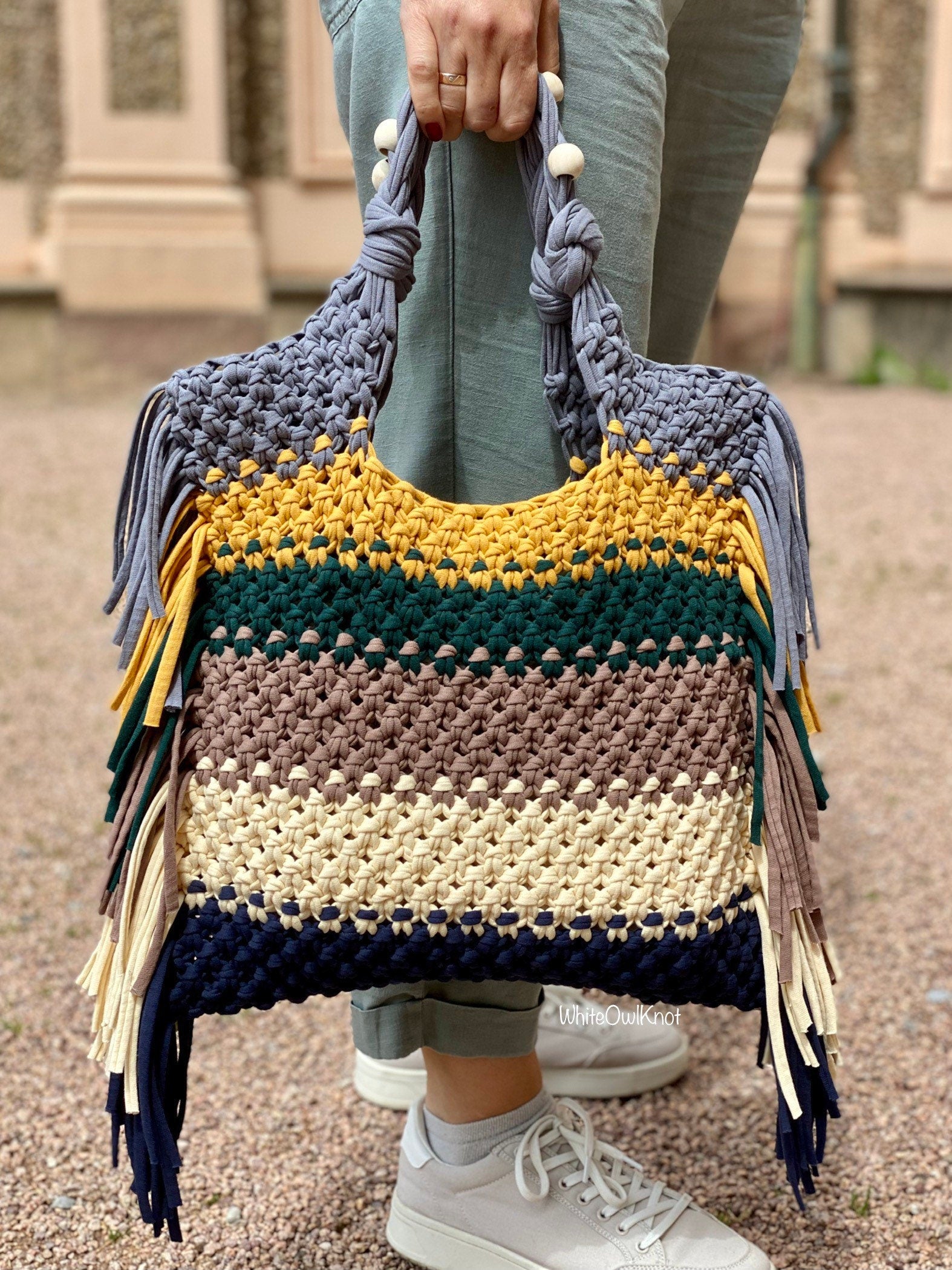 Colorful macrame handbag with fringes held by a person outdoors.