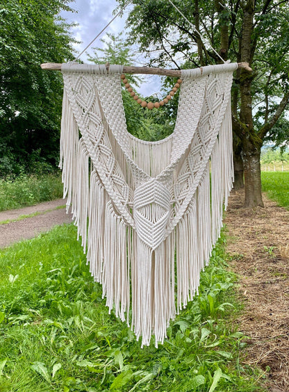 Macrame wall hanging with fringe hanging outdoors on a tree branch.