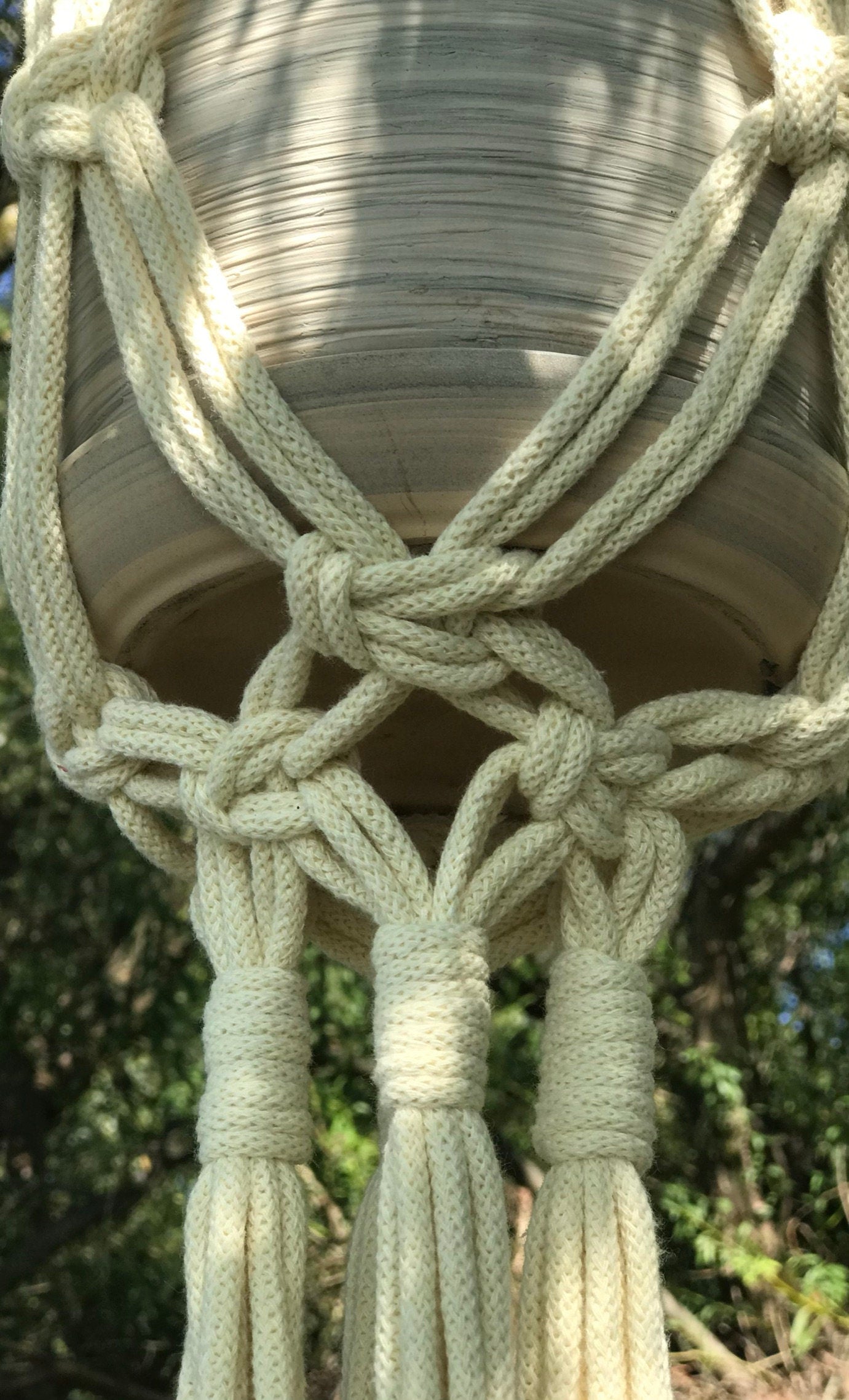 Close-up of a macrame plant hanger with natural light and blurred greenery in the background.