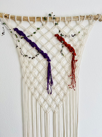 Macrame wall hanging with purple and red braided ends on a white background
