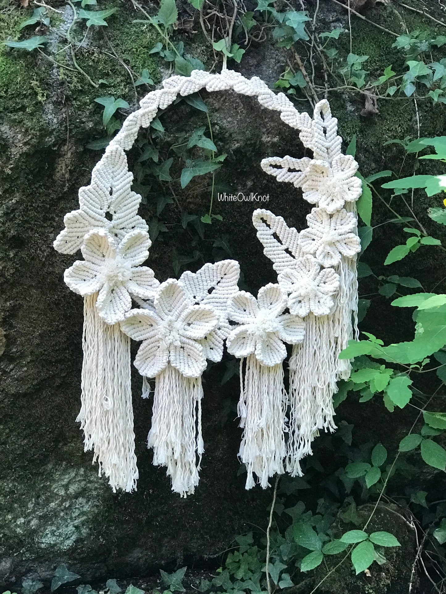 Decorative wall hanging with floral designs and tassels against a natural stone background