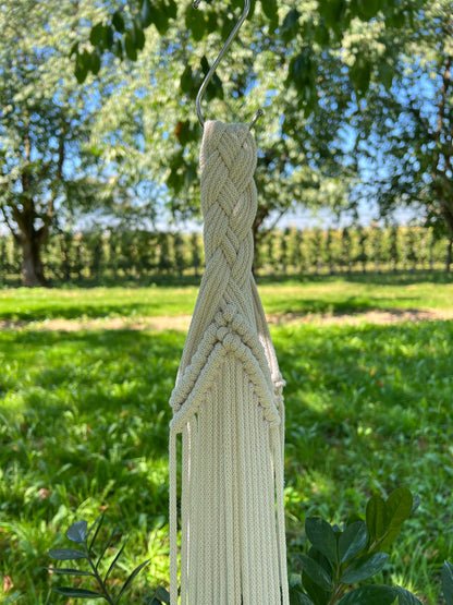 Macrame plant hanger hanging outdoors with greenery in the background