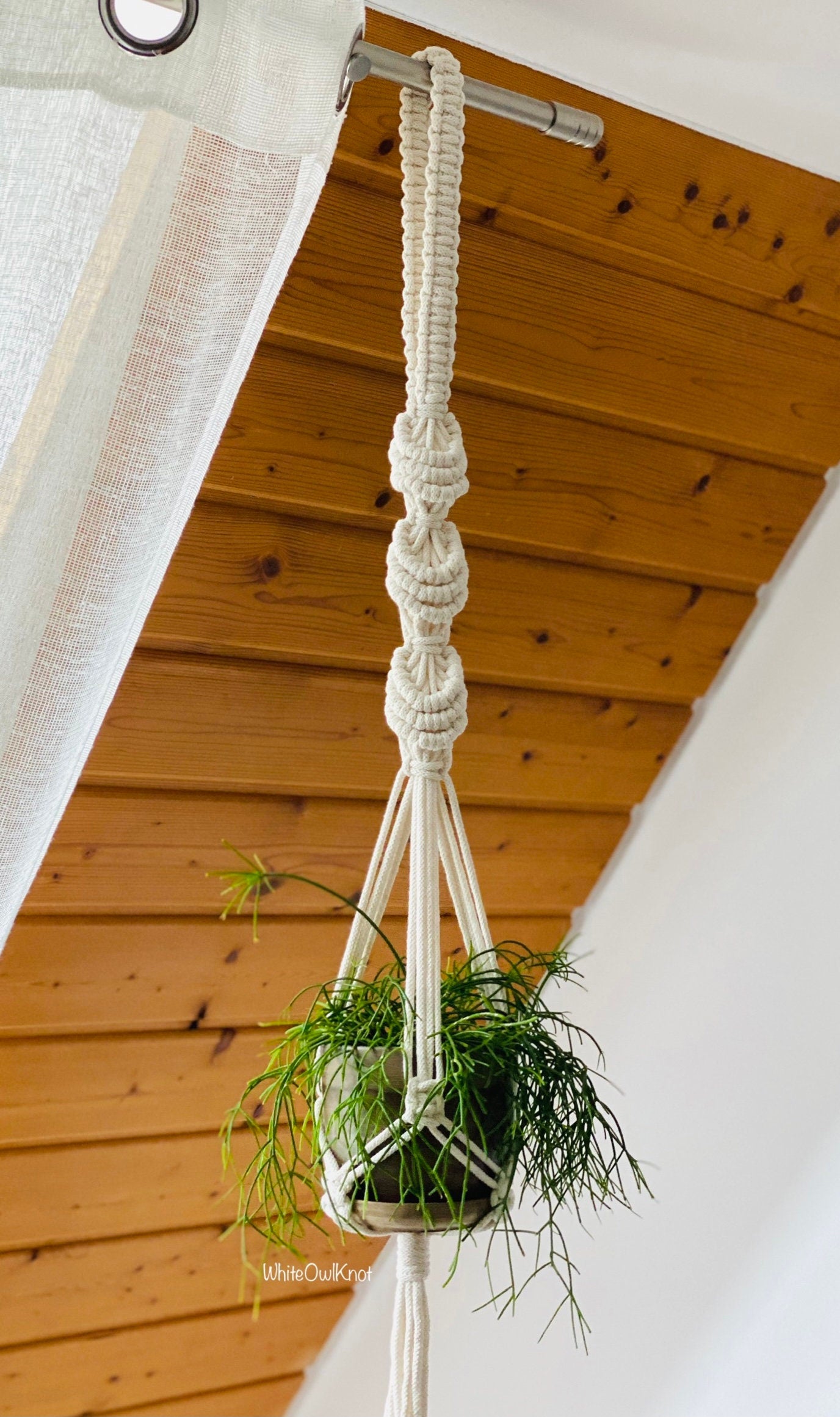 Macrame plant hanger with a plant against a wooden ceiling