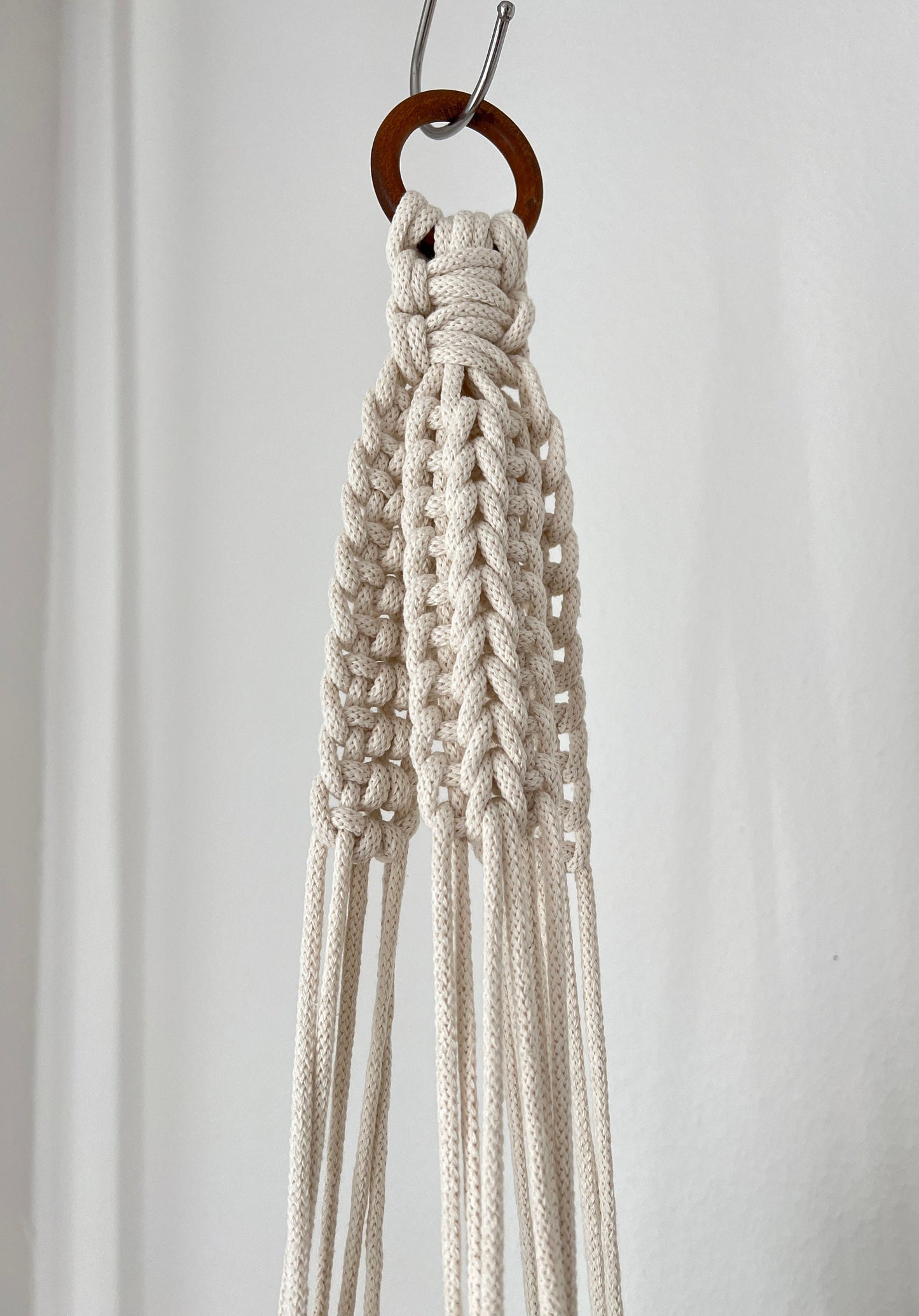 Macrame plant hanger hanging on a hook against a plain background