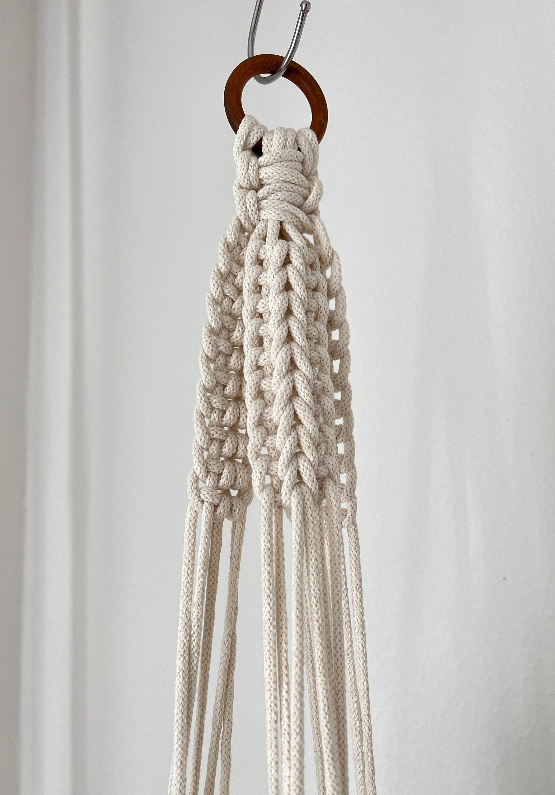 Macrame plant hanger hanging on a hook against a plain background