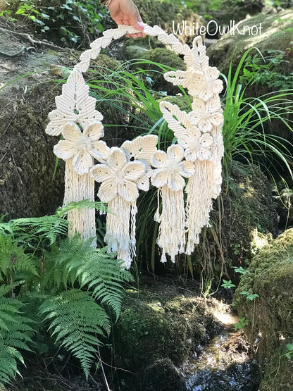 Macrame wall hanging with floral designs and tassels in a natural setting.