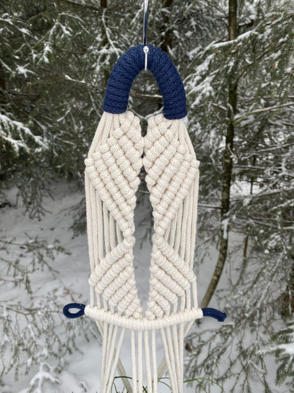 Macrame wall hanging with blue accents against a snowy forest background