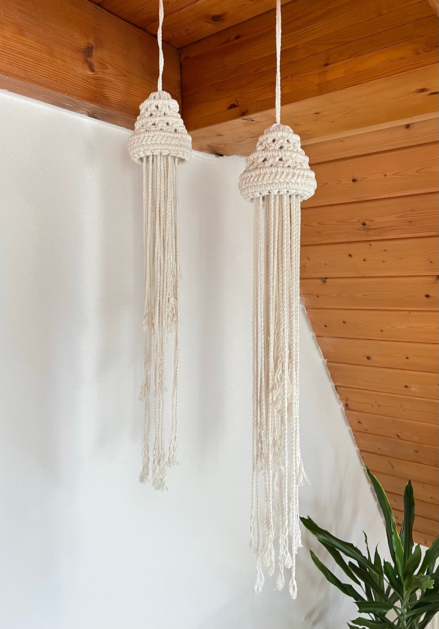 Two macrame hanging jellyfish against a wooden ceiling and white wall.