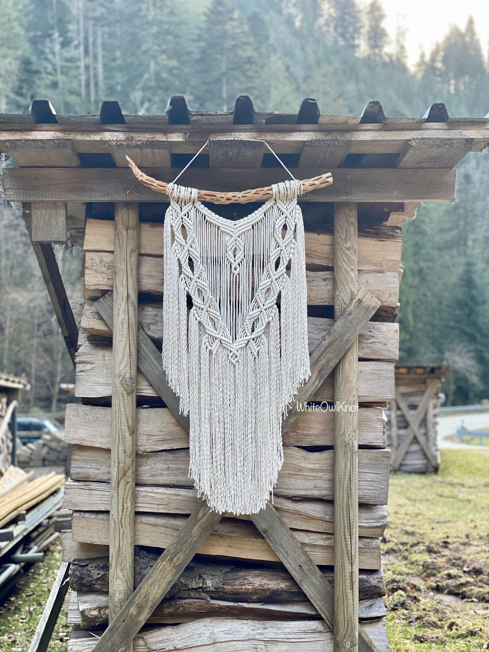 Macrame wall hanging on a wooden structure outdoors with trees in the background