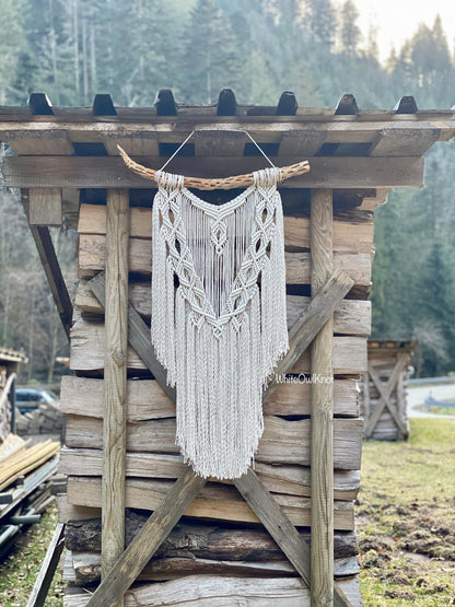 Macrame wall hanging on a wooden structure outdoors with trees in the background