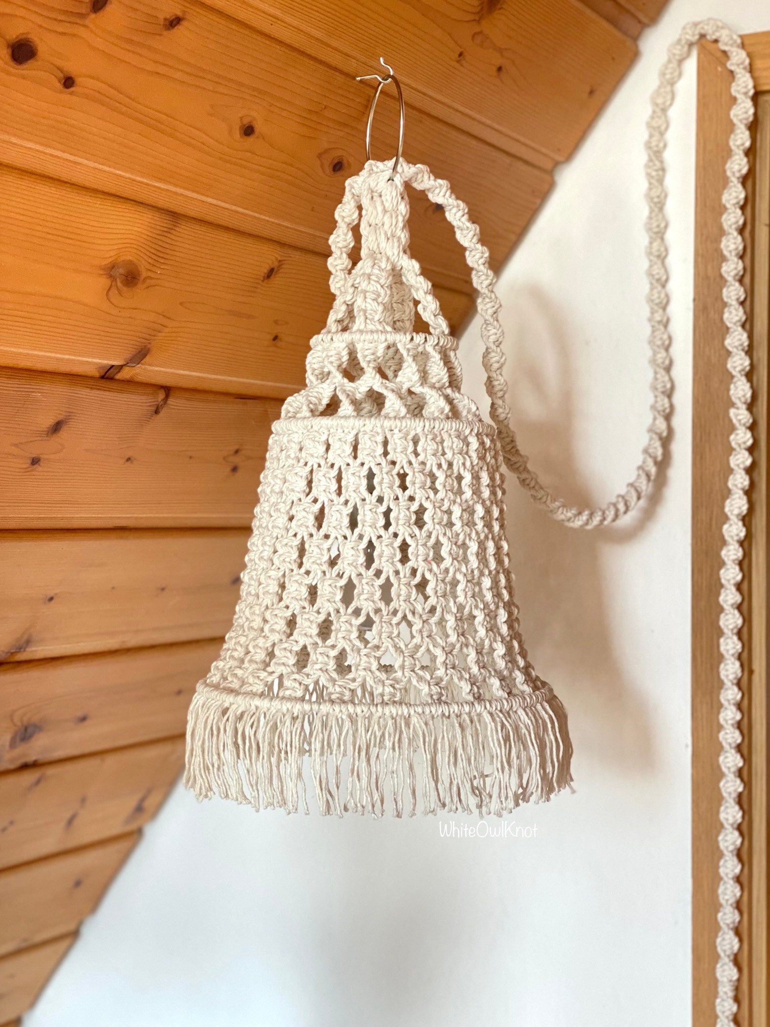 Macrame lamp shade with geometric pattern against a wooden wall.