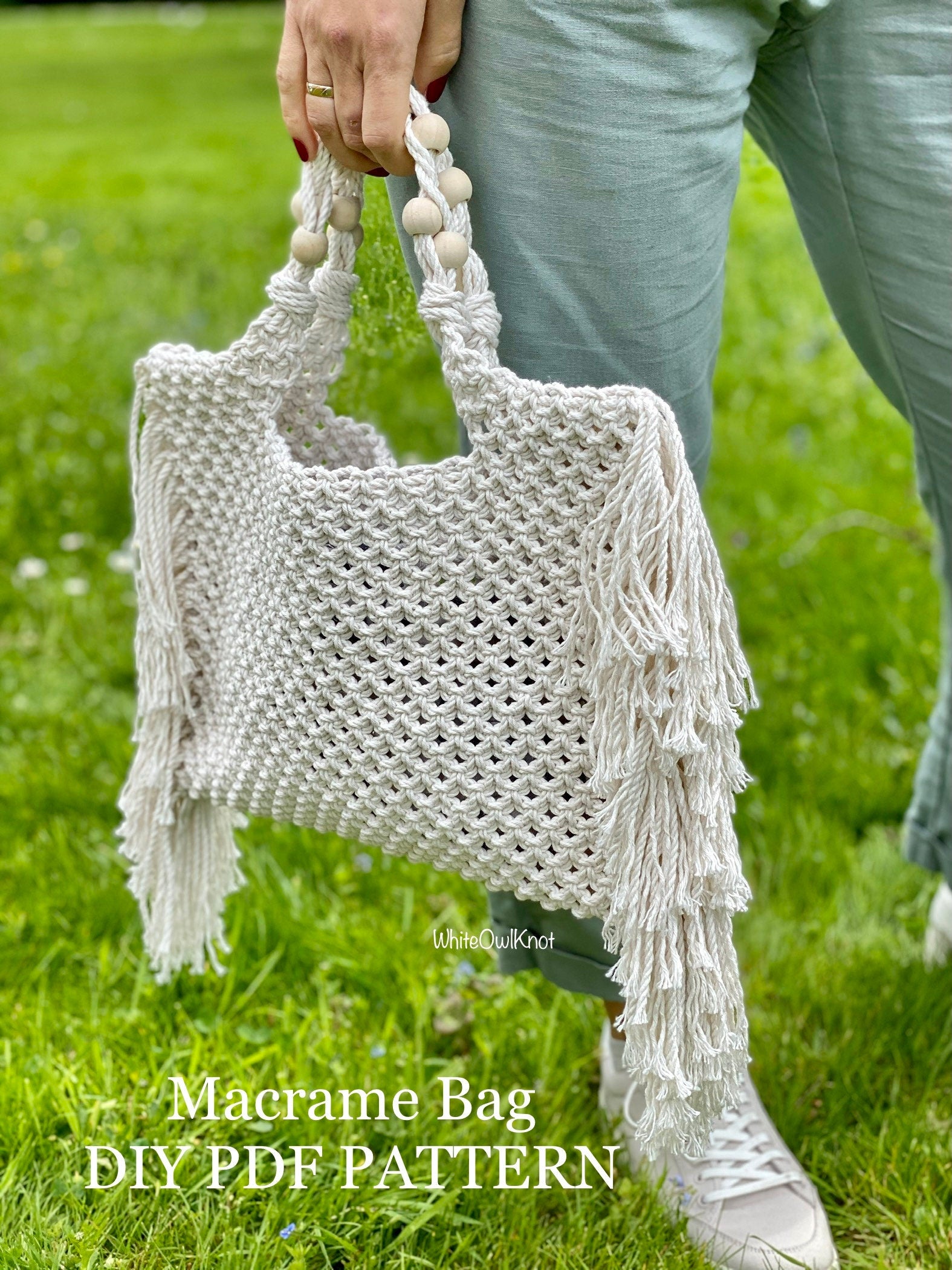 White macrame bag with fringe held by a person on grass