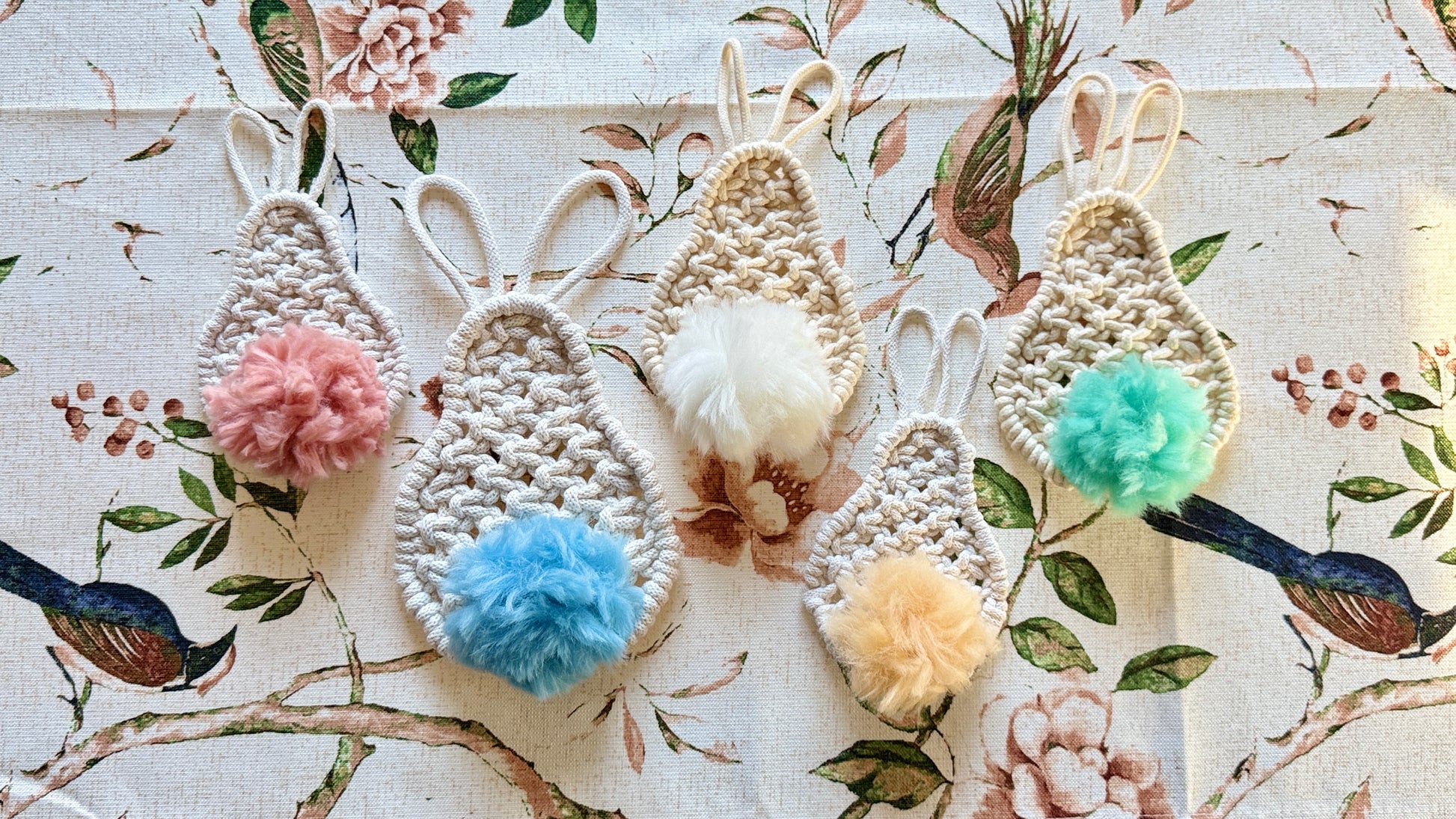 Macrame easter bunnies with colorful pom-poms on a floral background