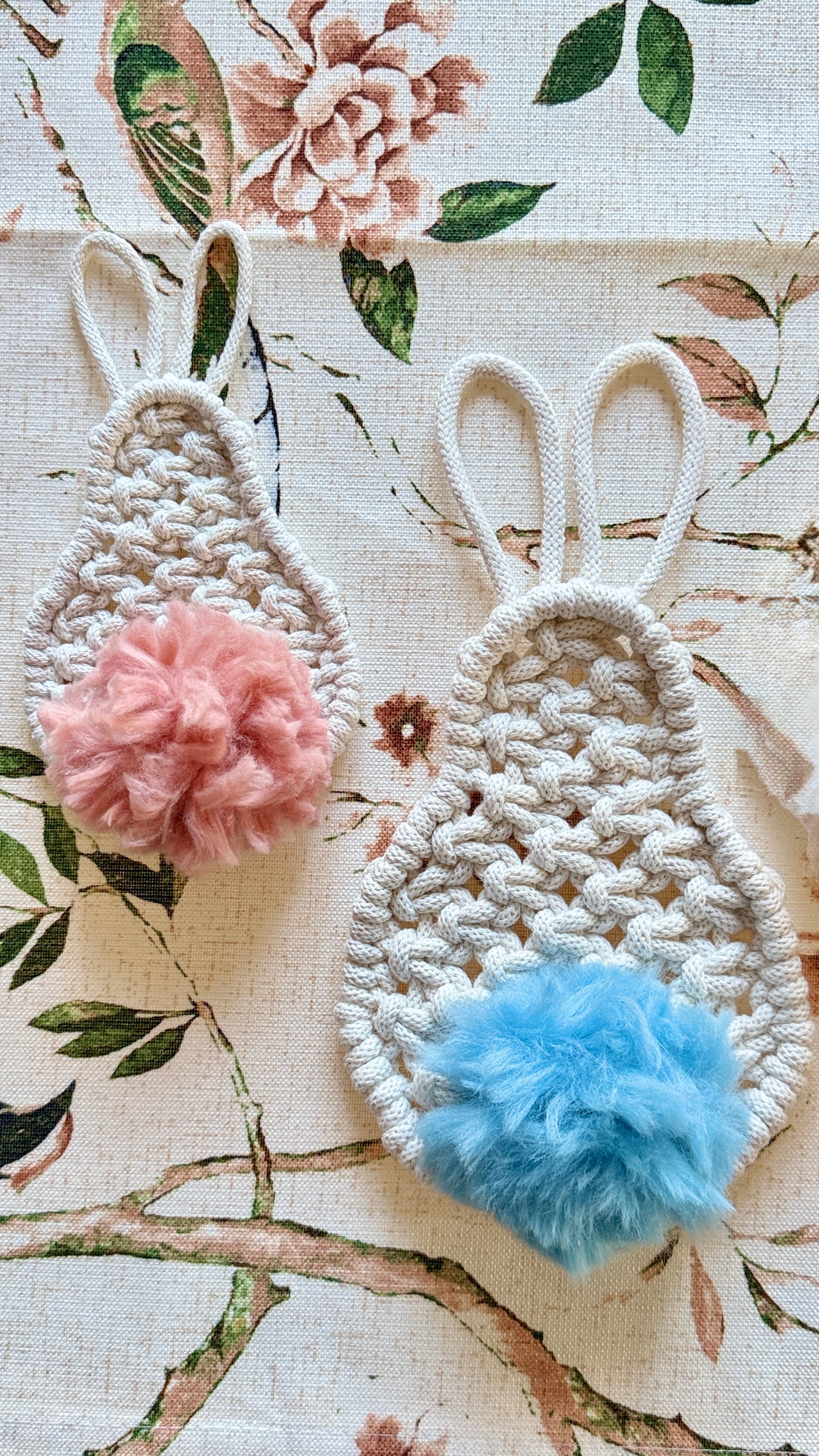 Two macramebunny ears with pom-poms on a floral background