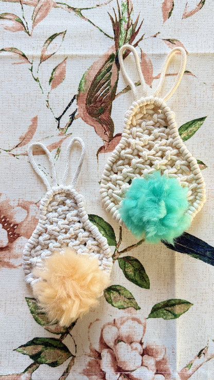 Two decorative macrame easter bunnies with pom-poms on a floral fabric background