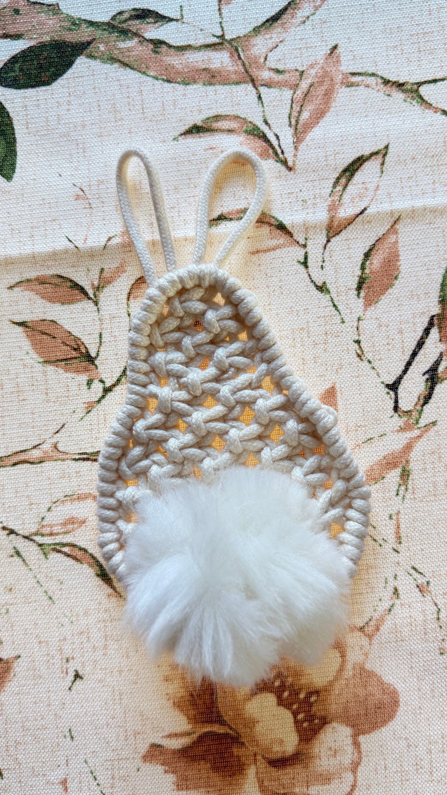 Handmade macrame bunny with a white pom-pom on a floral fabric background