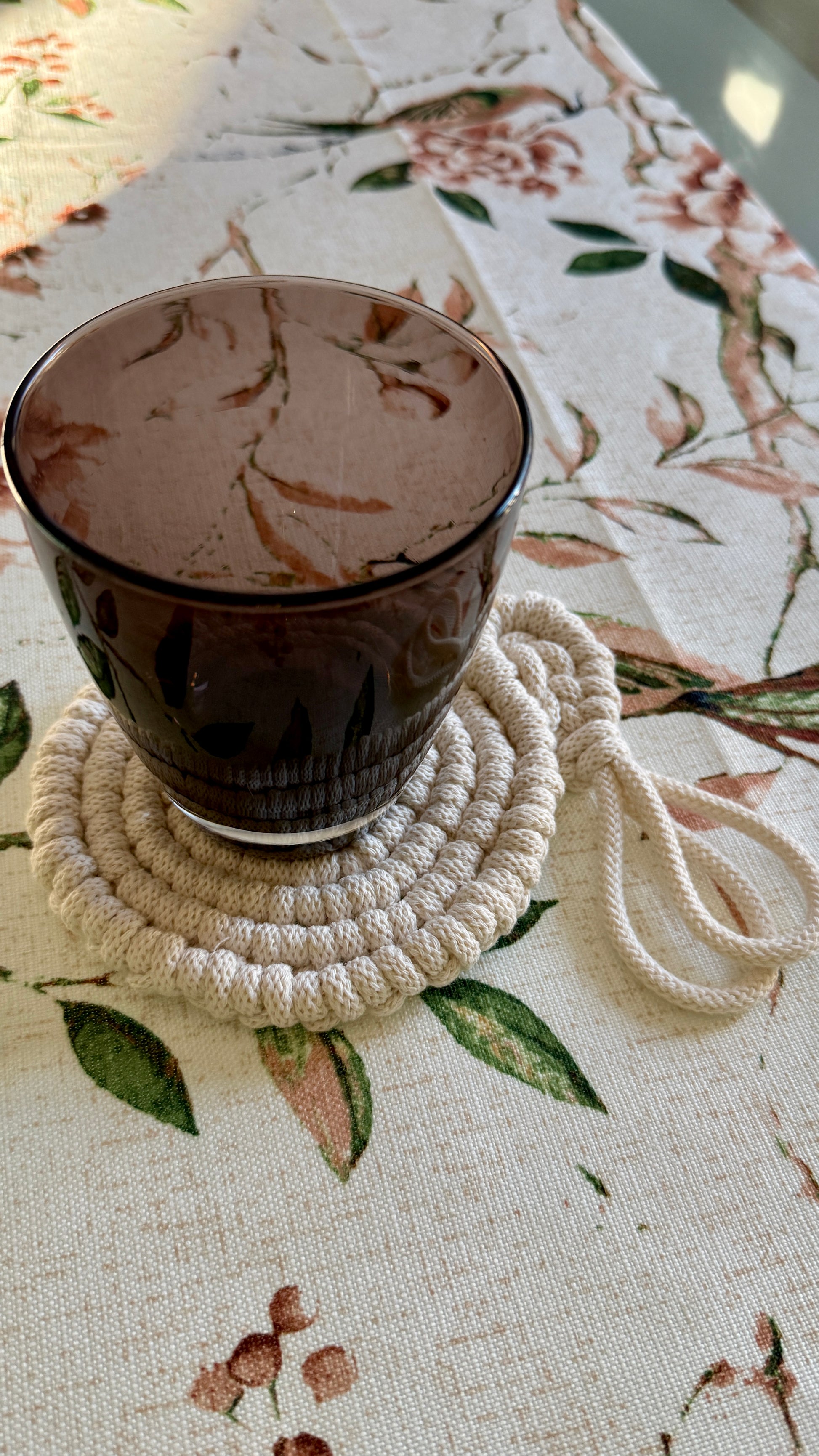 Black mug on a white rope coaster with a floral tablecloth background