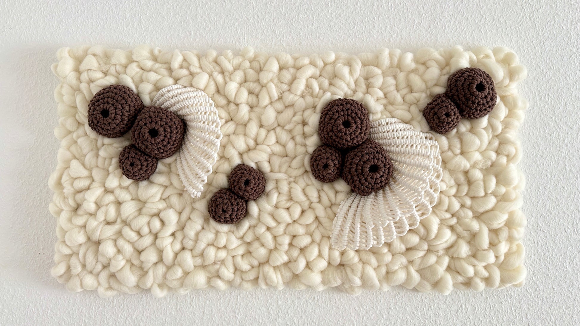 Textured white wall tapestry with brown crochet coral elements and white lace on a light gray background