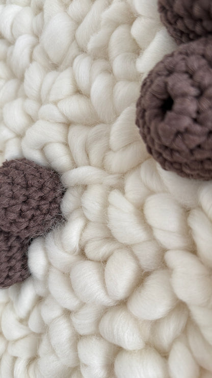 Close-up of textured white fabric with brown knitted balls.