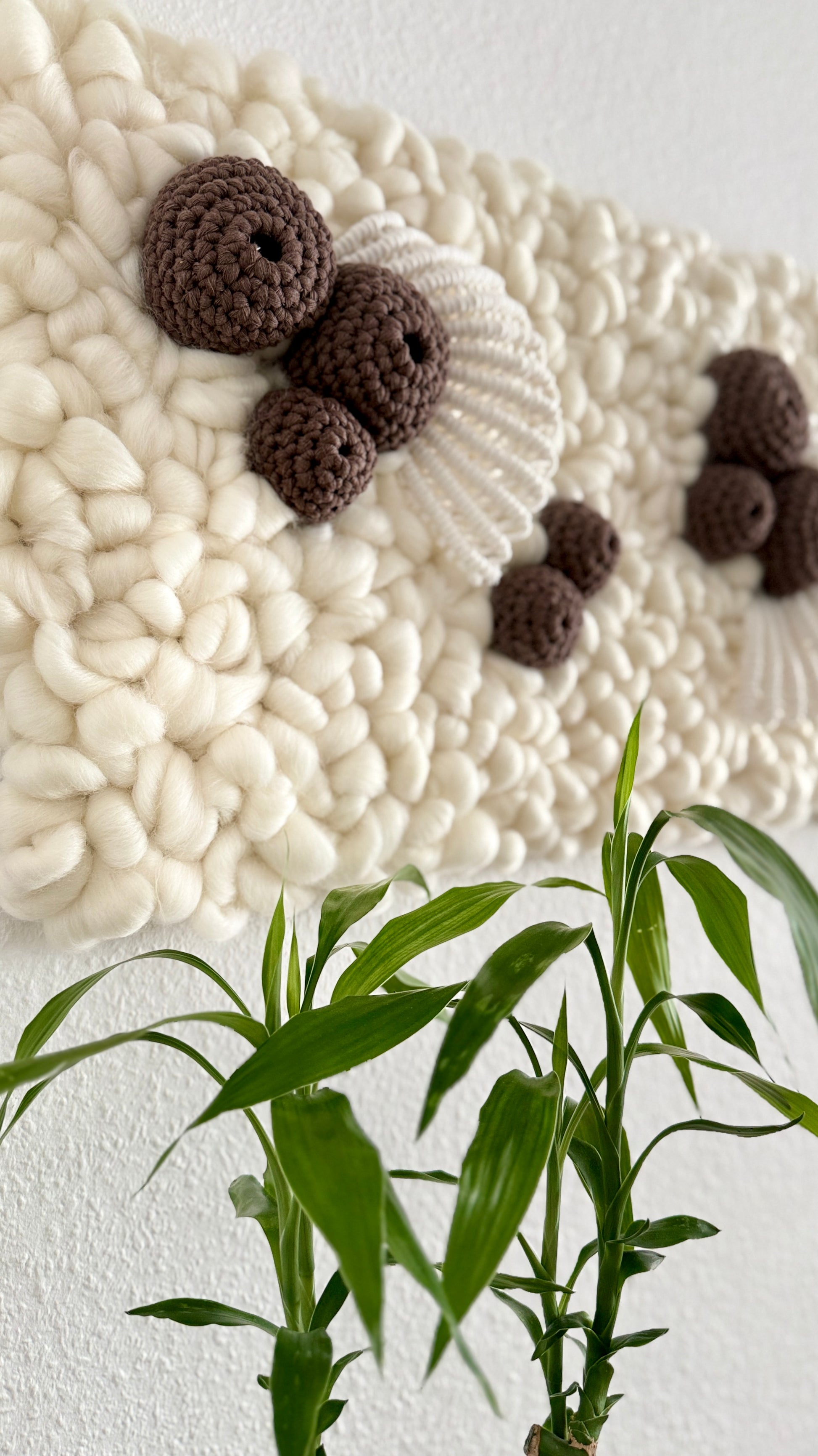 Textured wall art with brown spherical elements and white pebble pattern, accompanied by a plant.