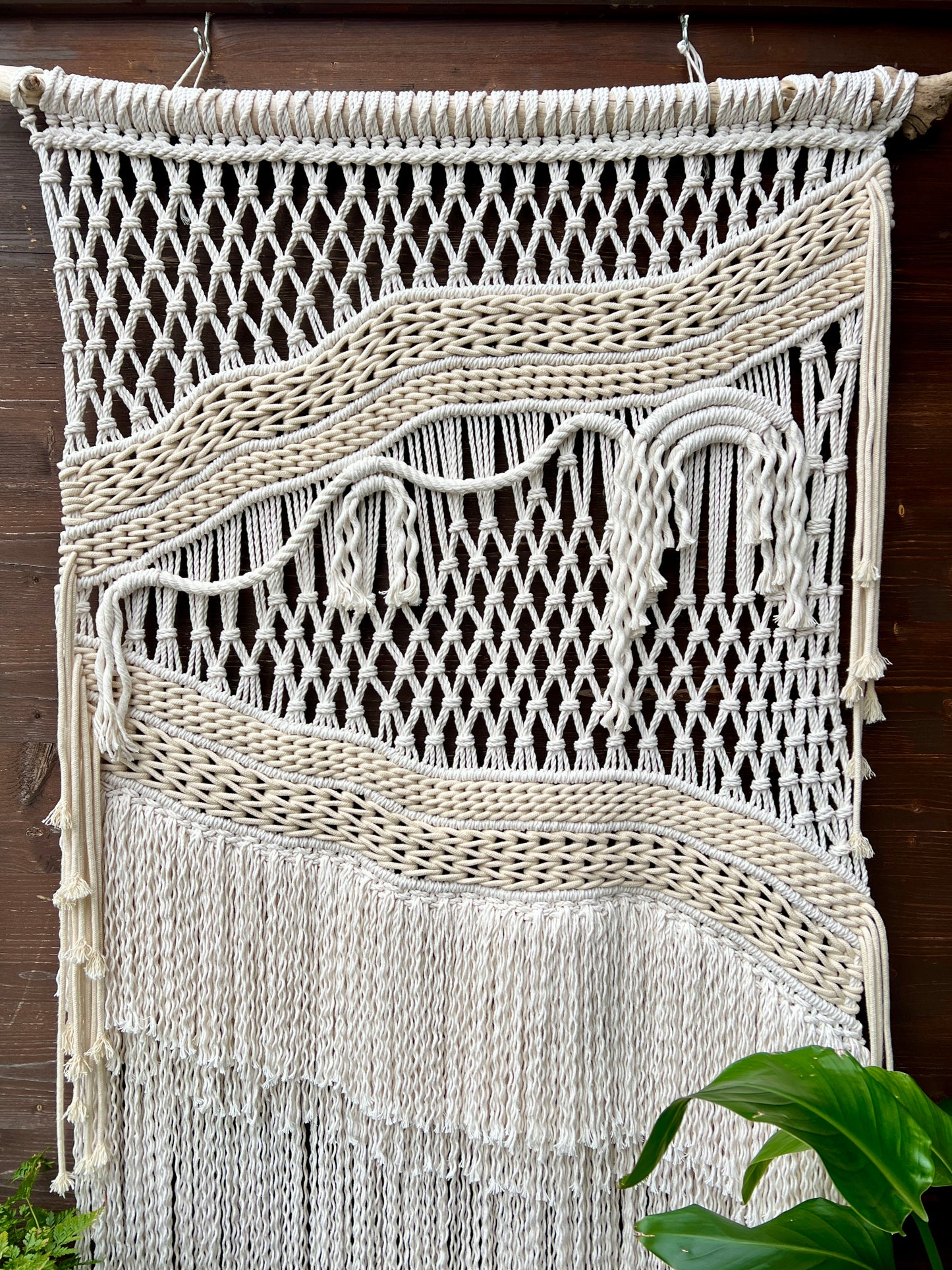 Macrame wall hanging with fringes on a wooden background