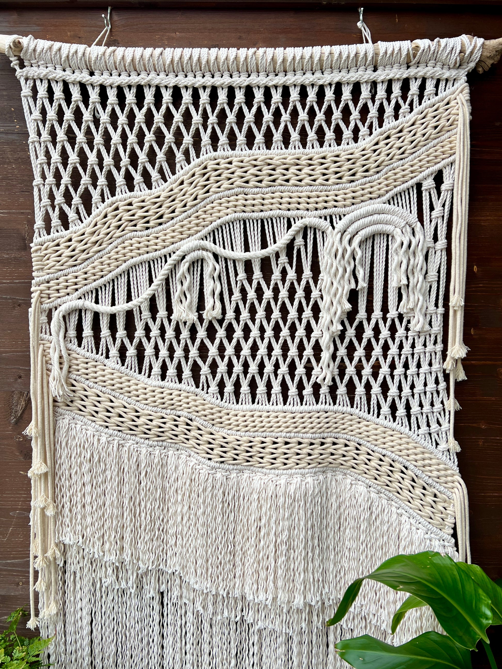 Macrame wall hanging with fringes on a wooden background