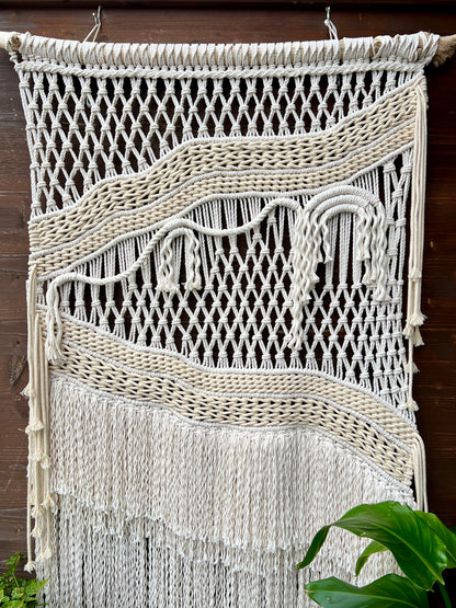 Macrame wall hanging with fringes on a wooden background