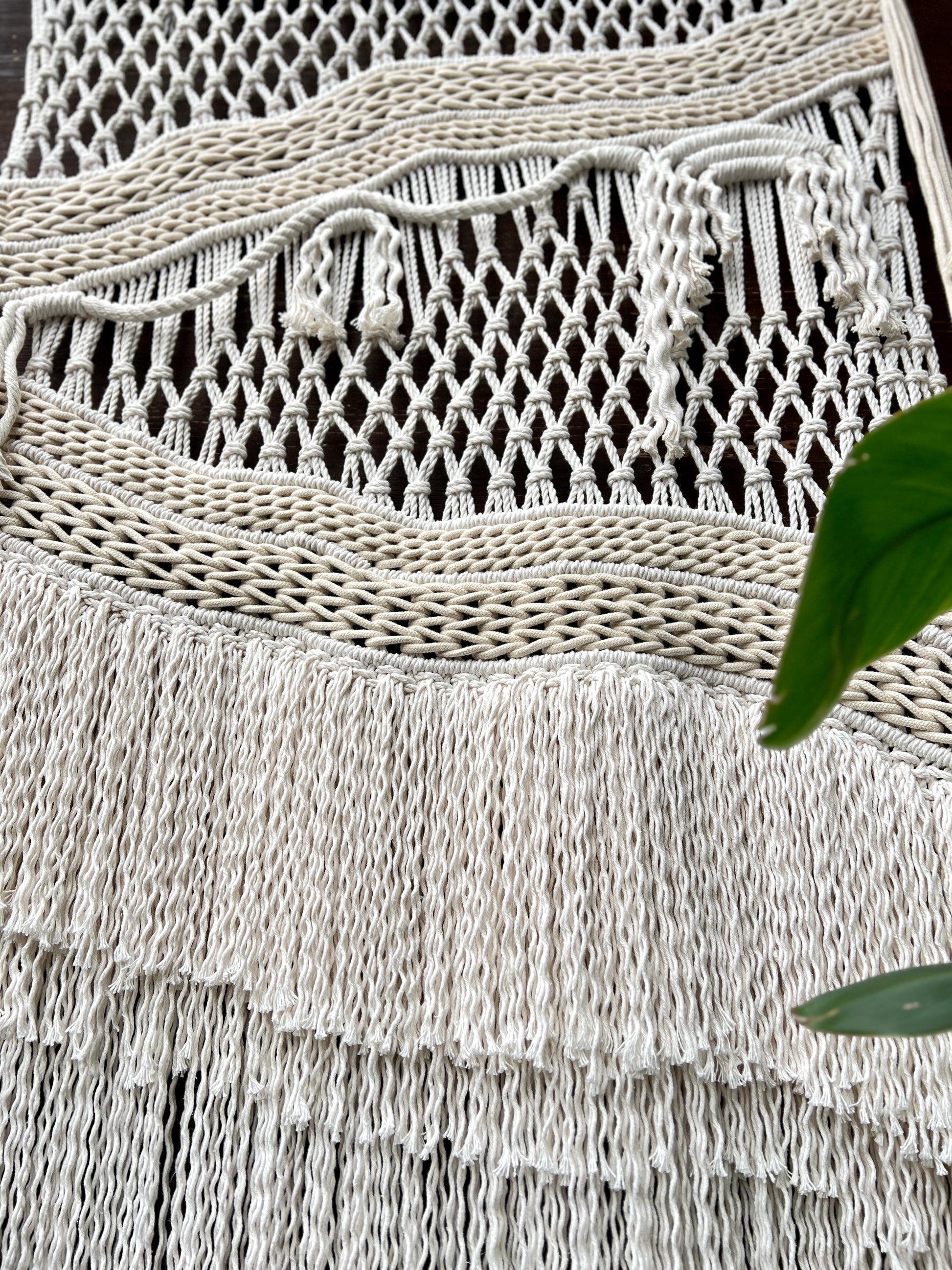 Close-up of a textured woven mat with fringe, partially covered by green leaves.