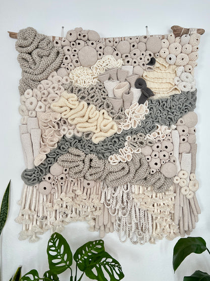 Textile art piece with coral reef details and textures on a white wall.