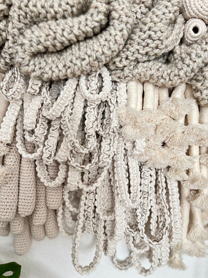 Close-up of textured beige fabric with fringes and a floral pattern.