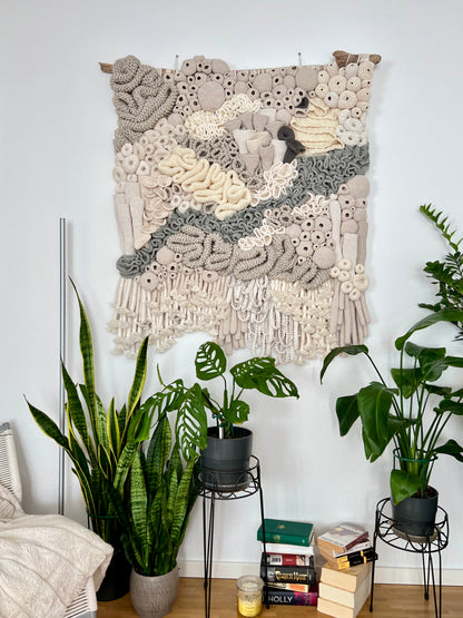 Textile art piece on a wall with plants and books below