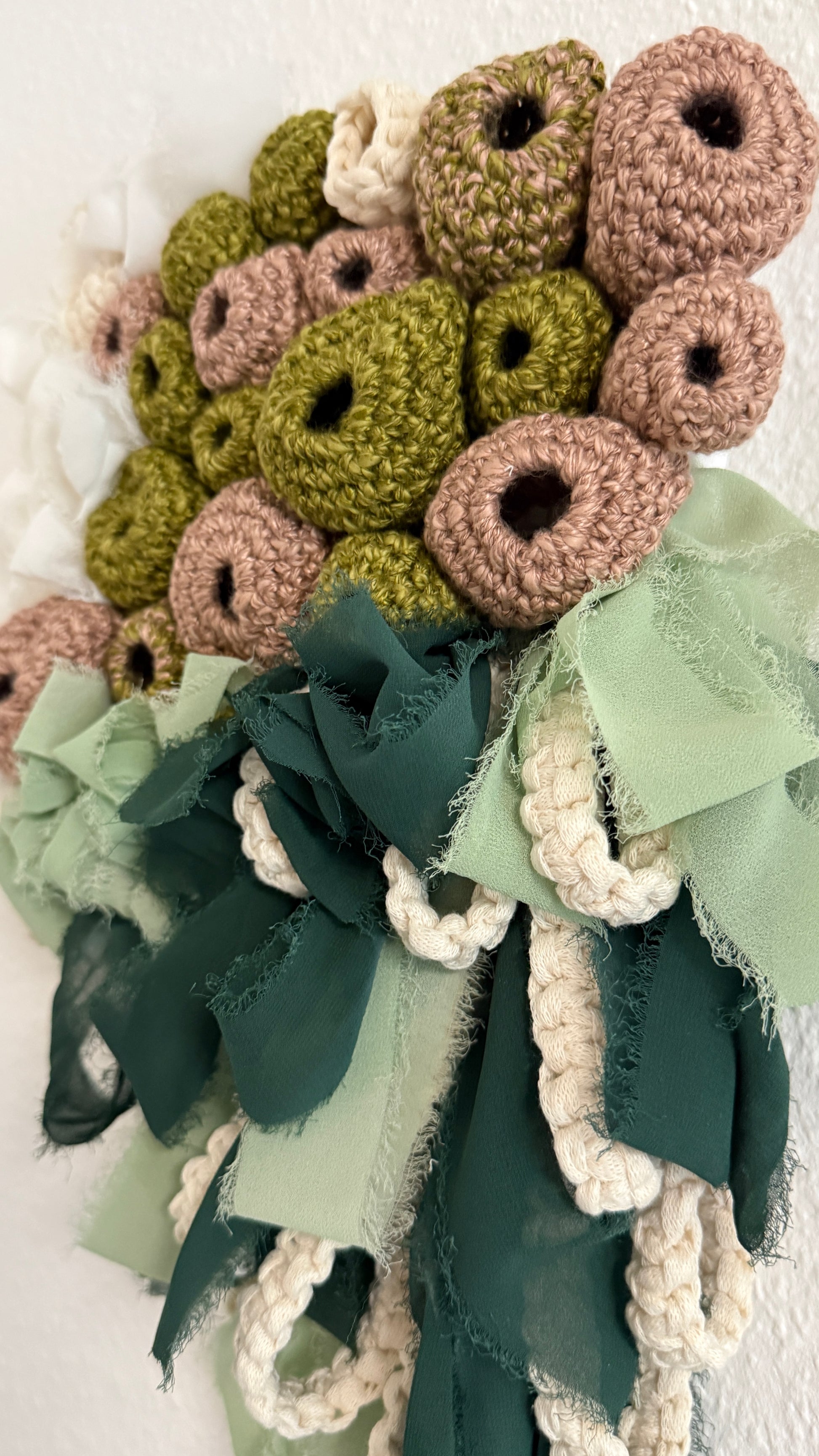 Crocheted flowers in green and brown with ribbons on a white background