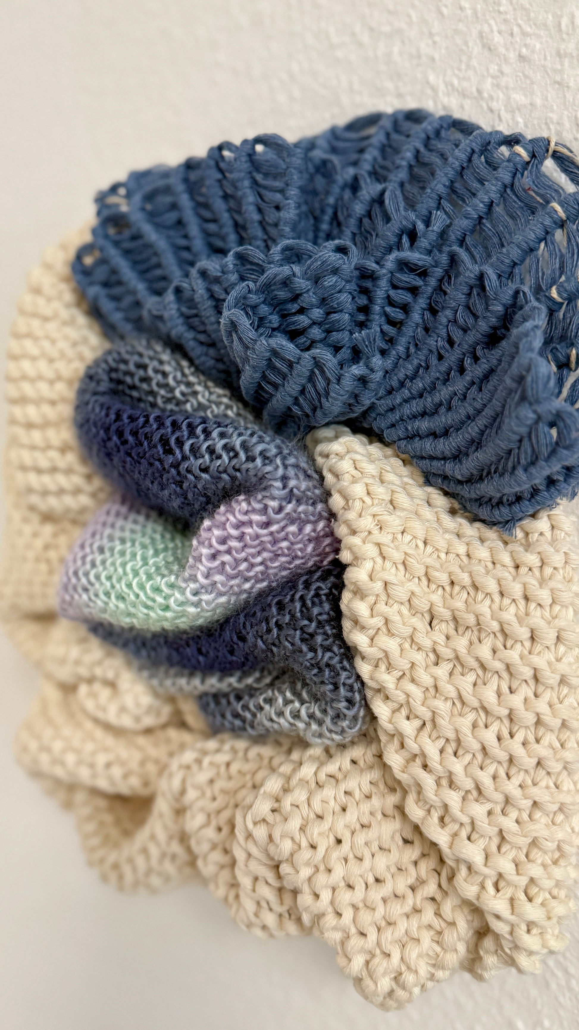 macrame details of wall hanging including a blue and beige elements and a purple and green yarn on a light background.