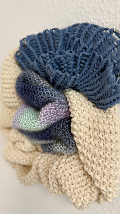 macrame details of wall hanging including a blue and beige elements and a purple and green yarn on a light background.