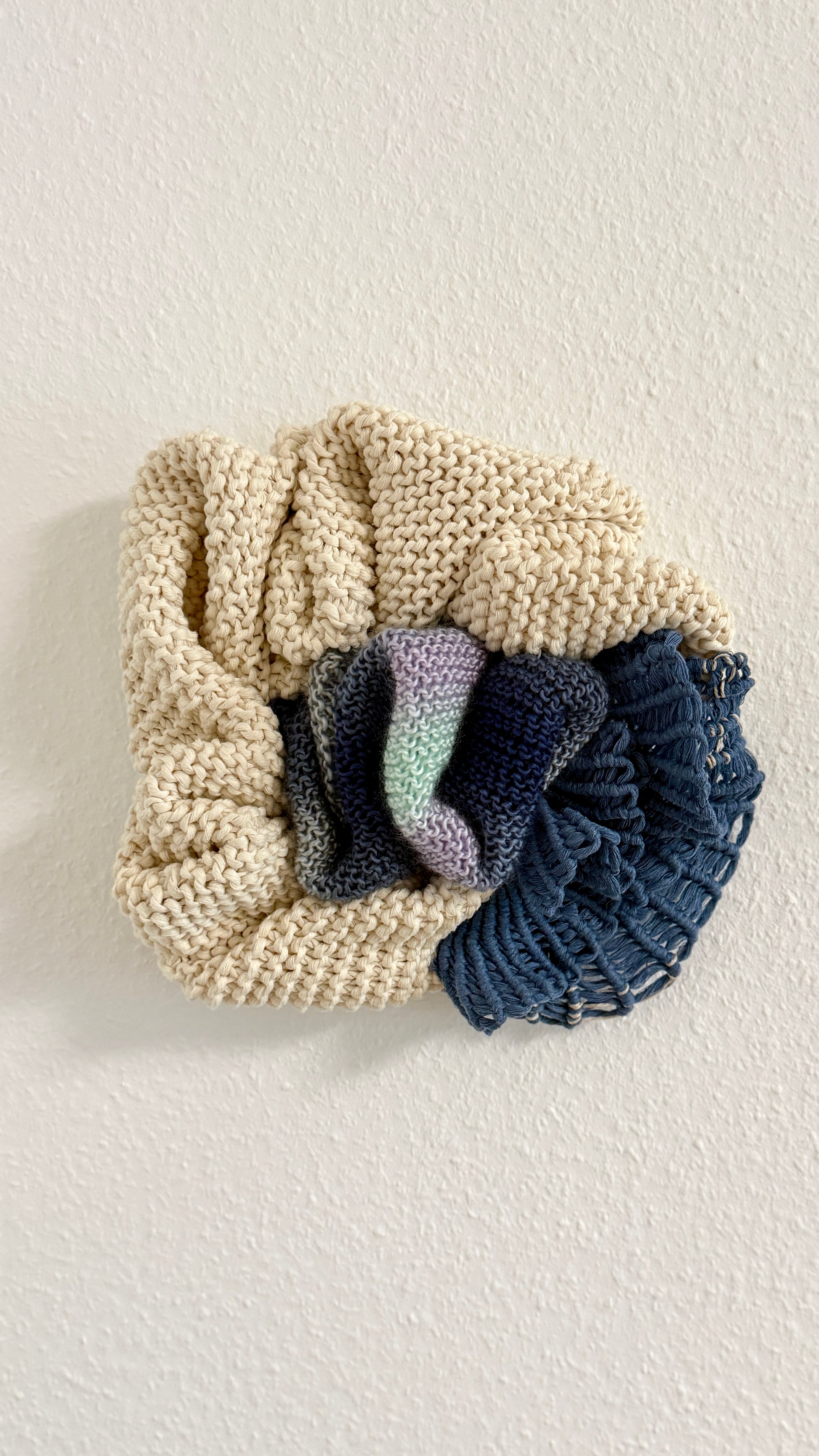 Knitted fiber art wall hanging on a light background