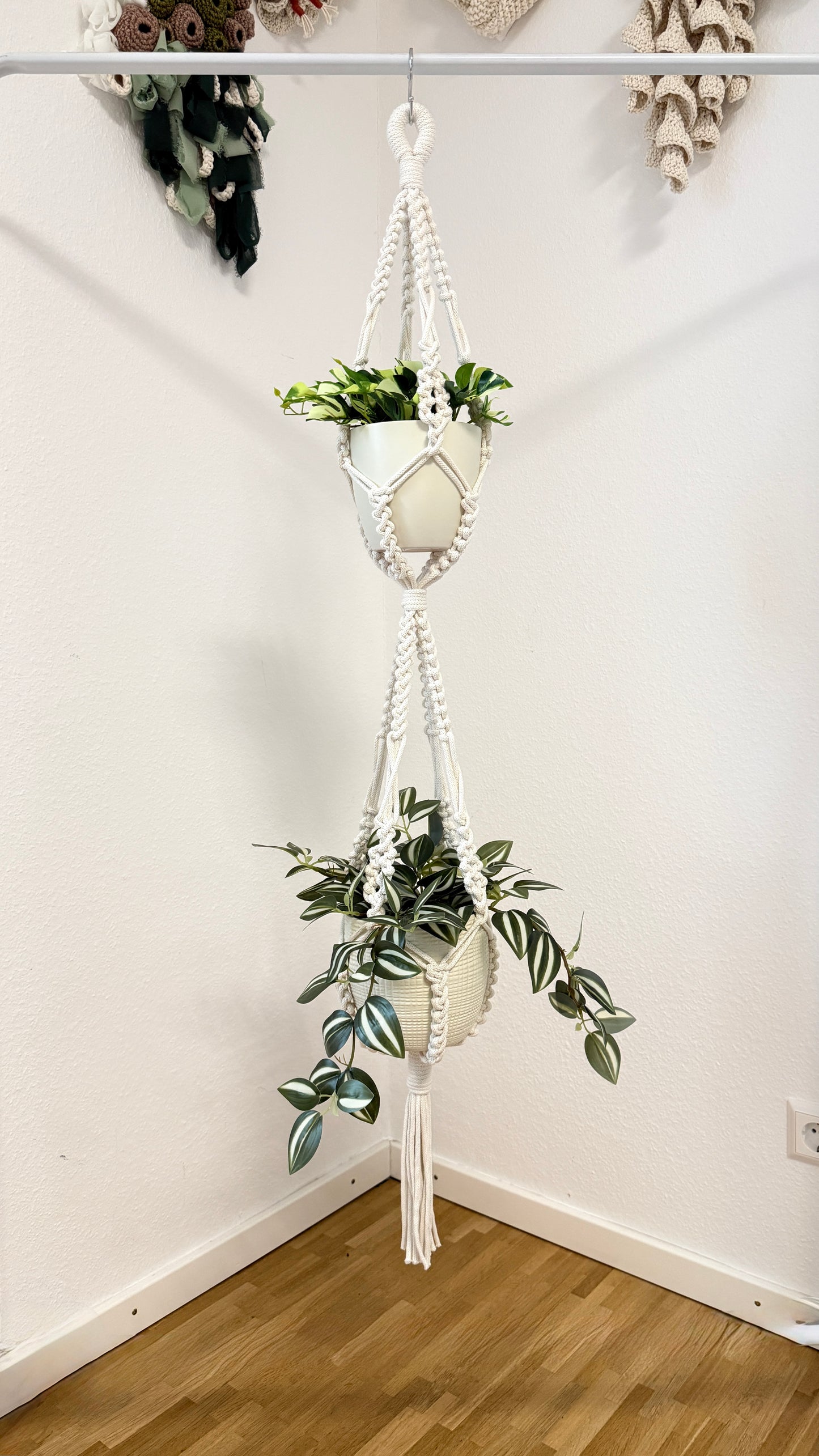 Macrame plant hanger with multiple plant pots against a white wall.