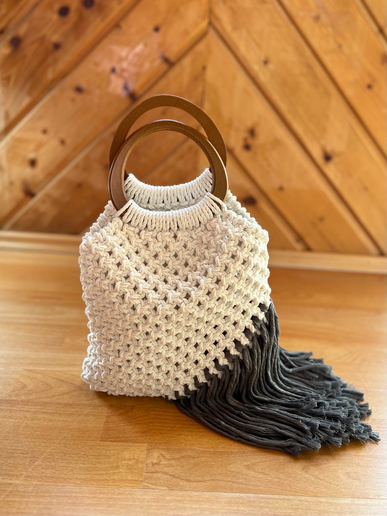 Macrame bag with wooden handles and grey tassel on a wooden surface