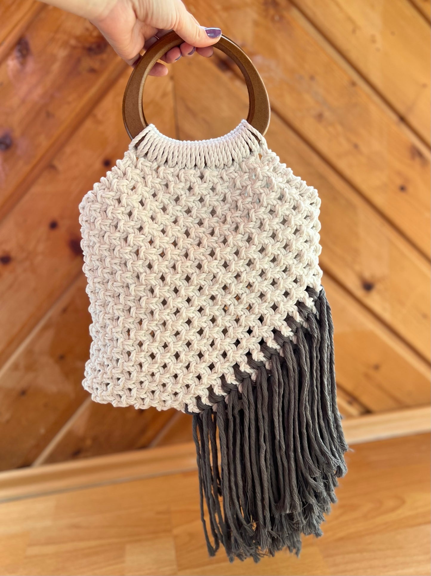 Handbag with a textured design and tassels held by a hand on a wooden floor.