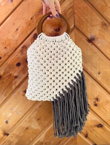 Handbag with wooden handle and fringe details held against a wooden background