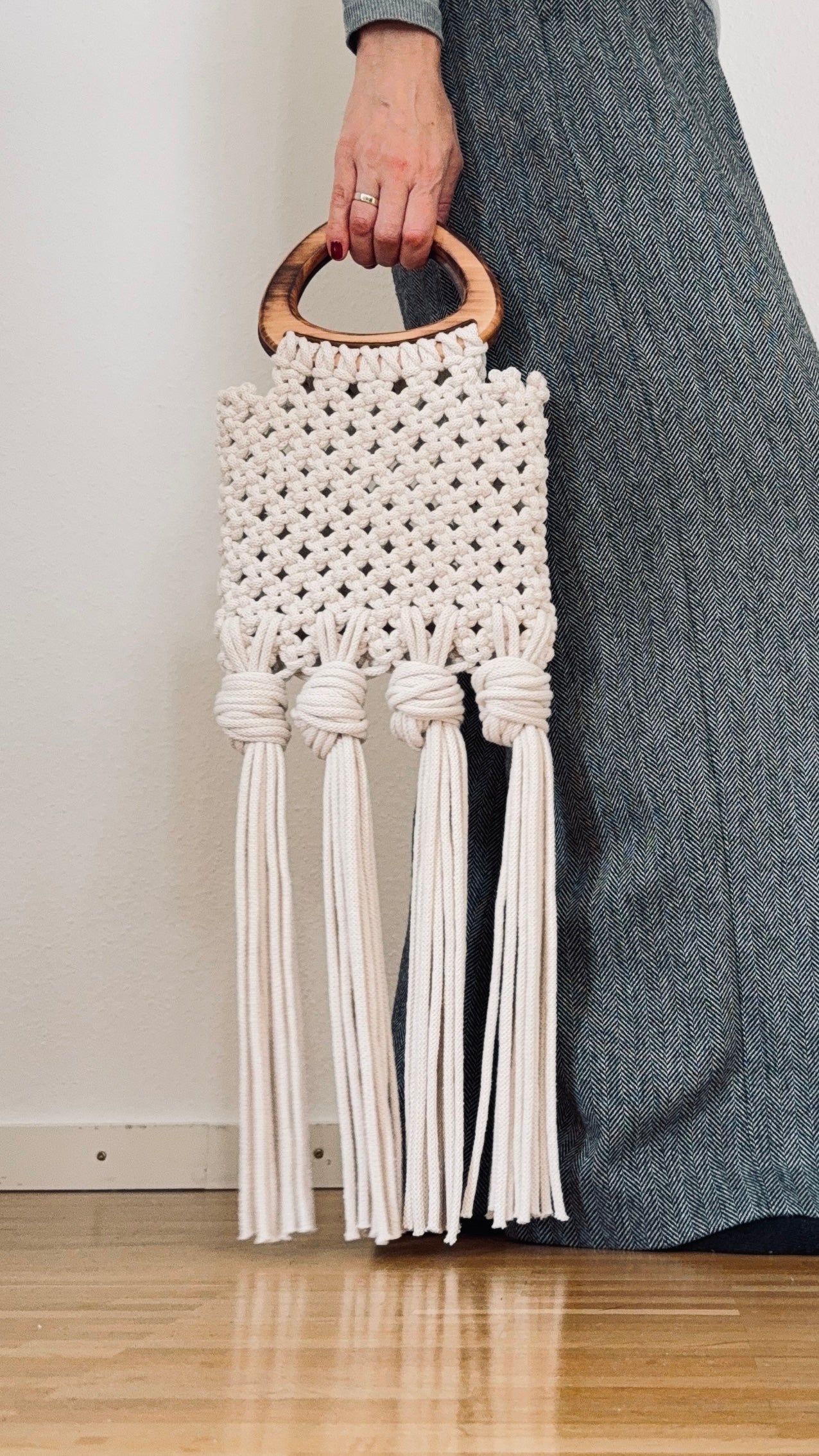 Macrame handbag with tassels held by a person wearing gray pants.